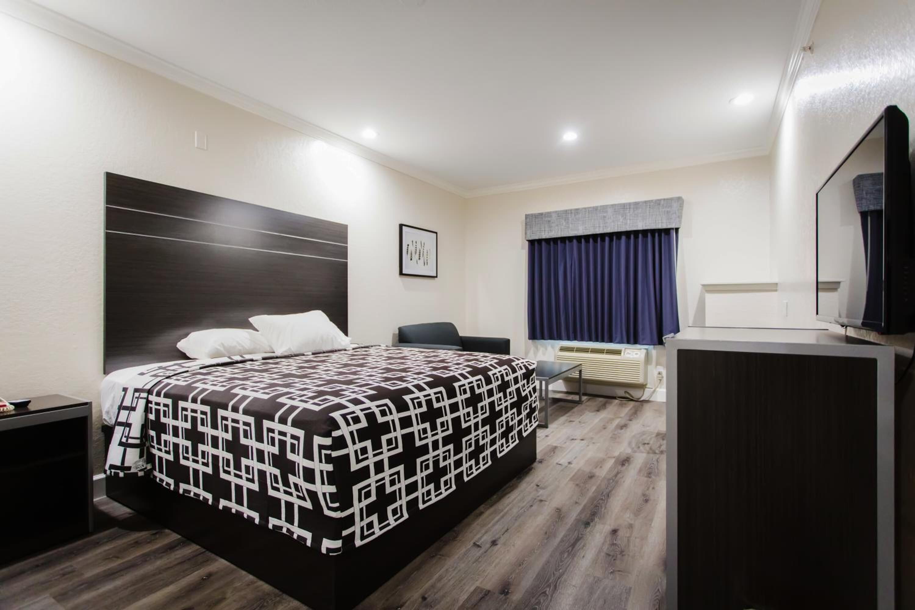 A hotel room with a bed, a desk, a chair, a television, and a window with curtains.