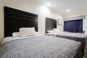 A hotel room with two beds, a large black headboard, a framed picture on the wall, and a window with blue curtains.