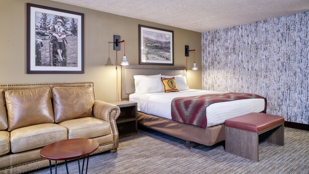 Una habitación de hotel con una cama, un sofá de cuero, una mesita y dos cuadros en la pared.