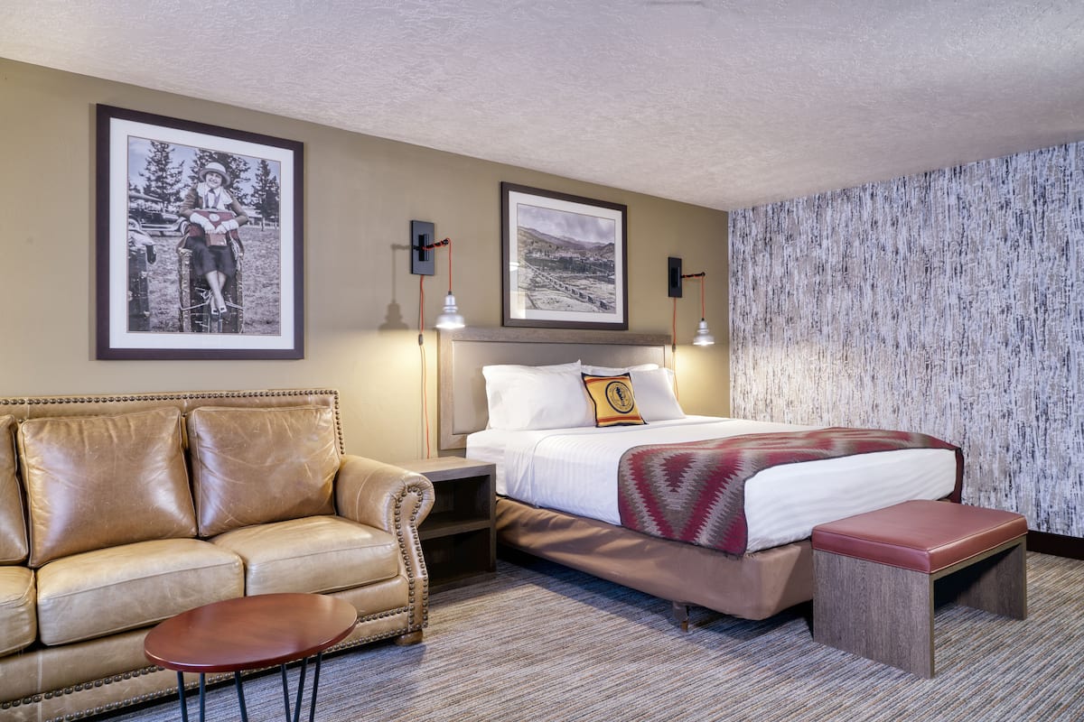 Une chambre d’hôtel avec un lit, un canapé en cuir, une petite table et deux tableaux encadrés au mur.