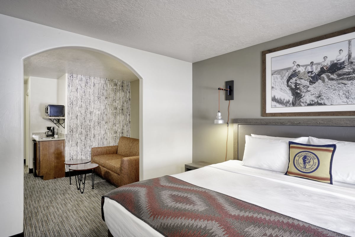 Une chambre d’hôtel avec un lit, un bureau avec un ordinateur, une chaise, une petite table et un tableau encadré au mur.
