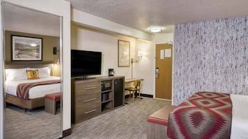 Habitación de hotel con cama, escritorio, televisión, microondas y un pequeño rincón de descanso.