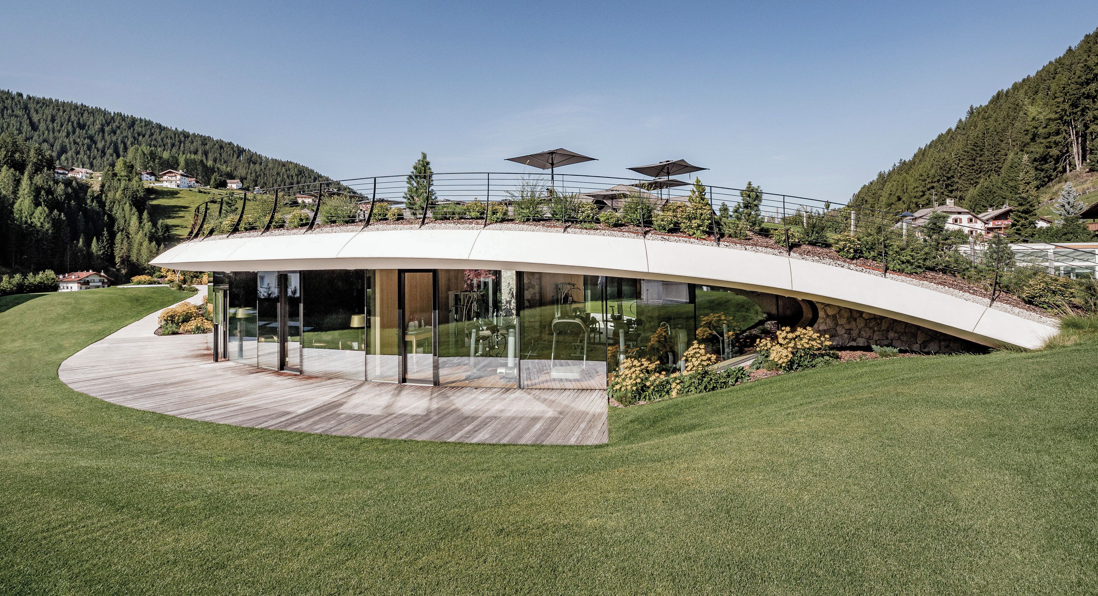 A modern building with a curved roof, large glass windows, and a wooden deck.