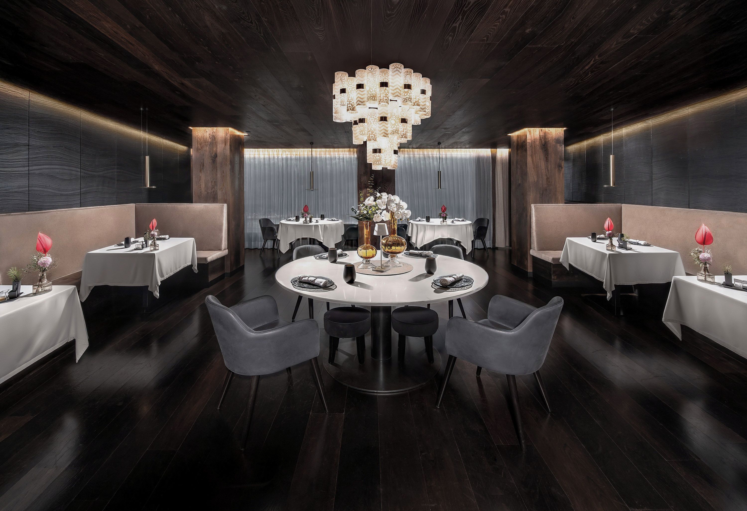 A modern dining area with round tables, dark wood flooring, and a central chandelier.