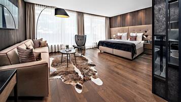 Une chambre d’hôtel moderne, équipée d’un canapé, d’un fauteuil, d’un lit, d’une petite table et d’une grande fenêtre avec des rideaux.