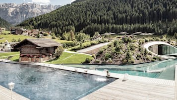 A pool area with a wooden deck, a small wooden cabin, and a modern building with a glass facade.