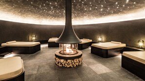 Een moderne spa met een centraal open haardelement, omringd door zitgedeeltes met kussens.