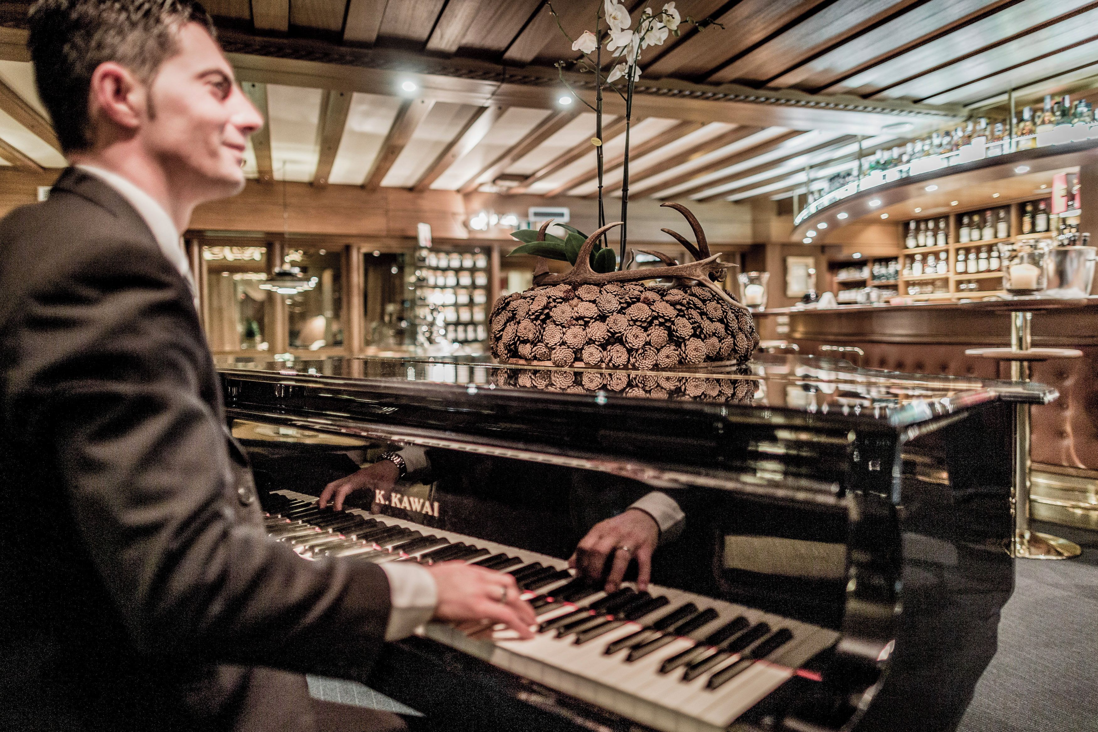 Eine Person spielt Klavier in einem Raum mit Holzwänden und einer Bar im Hintergrund.