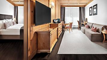 A hotel room with a bed, a TV, a desk, a sofa, and a dining area.