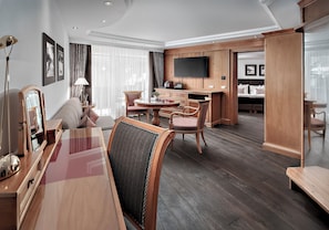 Een hotelkamer met een zithoek, een aan de muur bevestigde televisie en een groot raam met gordijnen.