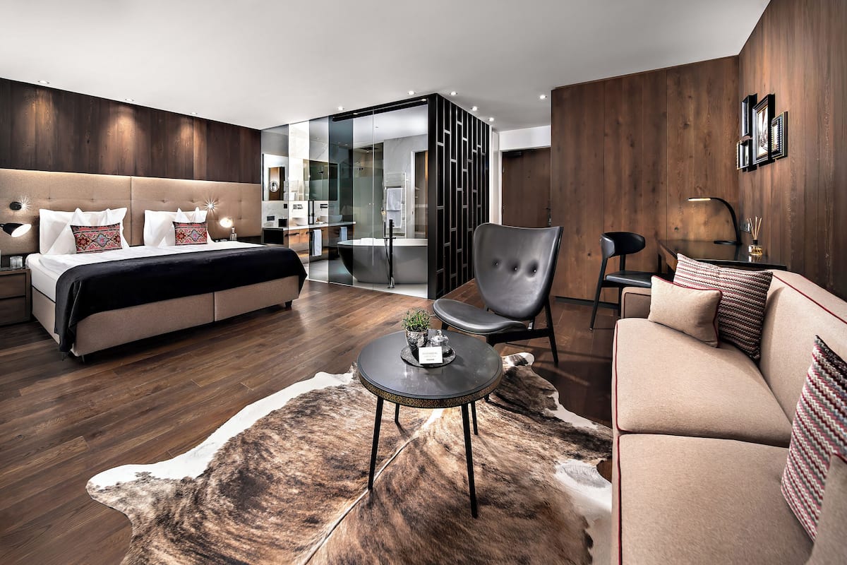 Een moderne hotelkamer met een bed, een slaapbank, een stoel, een bijzettafeltje en een glazen scheidingswand.