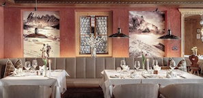 Een restaurant met een lange eettafel gedekt voor een maaltijd, een raam met uitzicht op bergen en een wand met een decoratief glaspaneel.