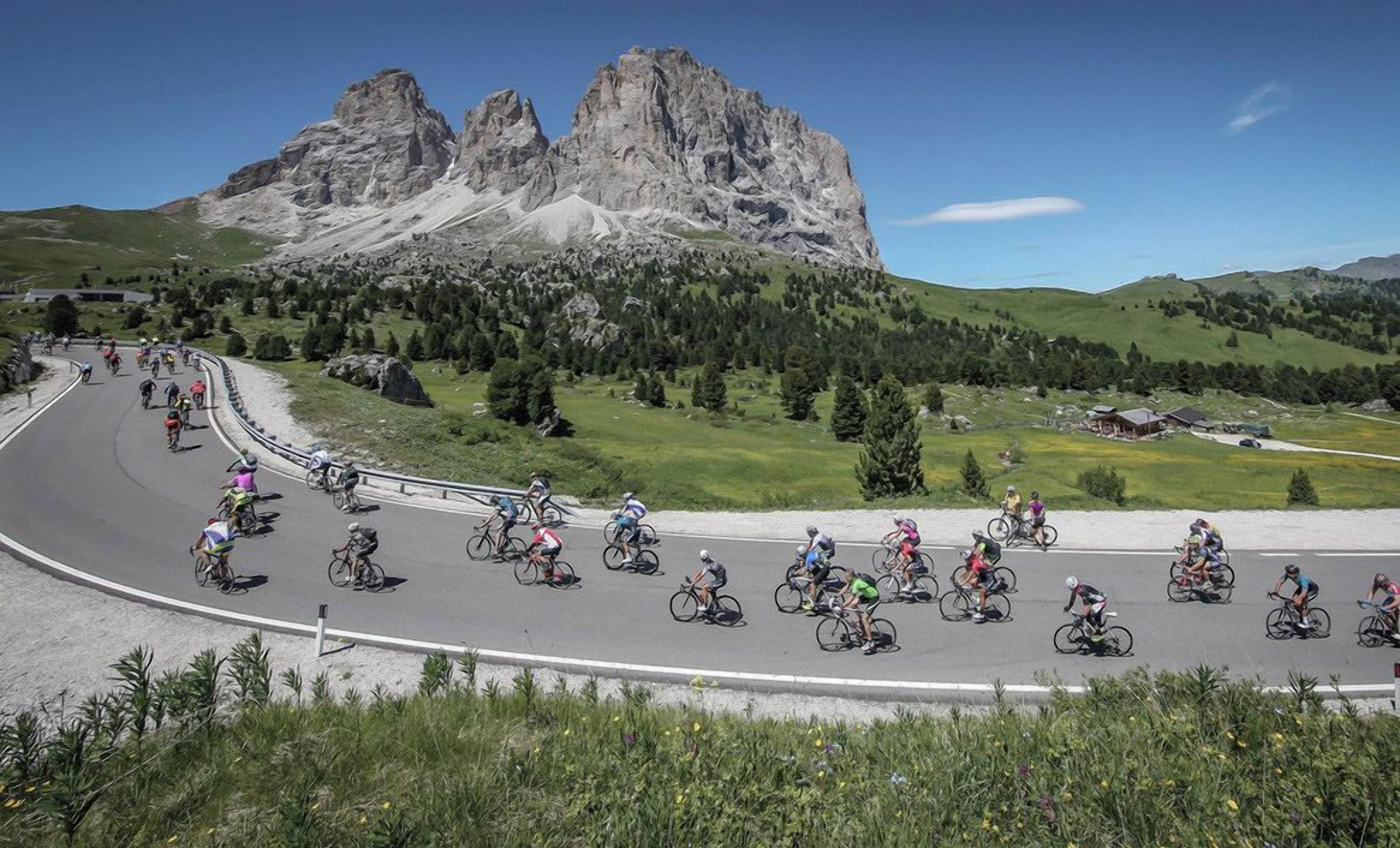 A group of cyclists on a winding road with a mountain backdrop.