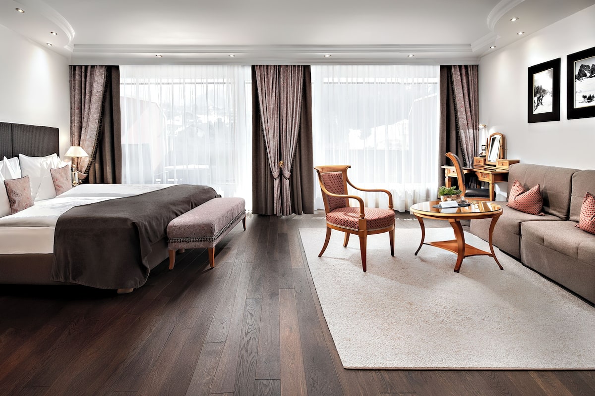 Een hotelkamer met een bed, een slaapbank, een stoel, een tafel en een groot raam met gordijnen.