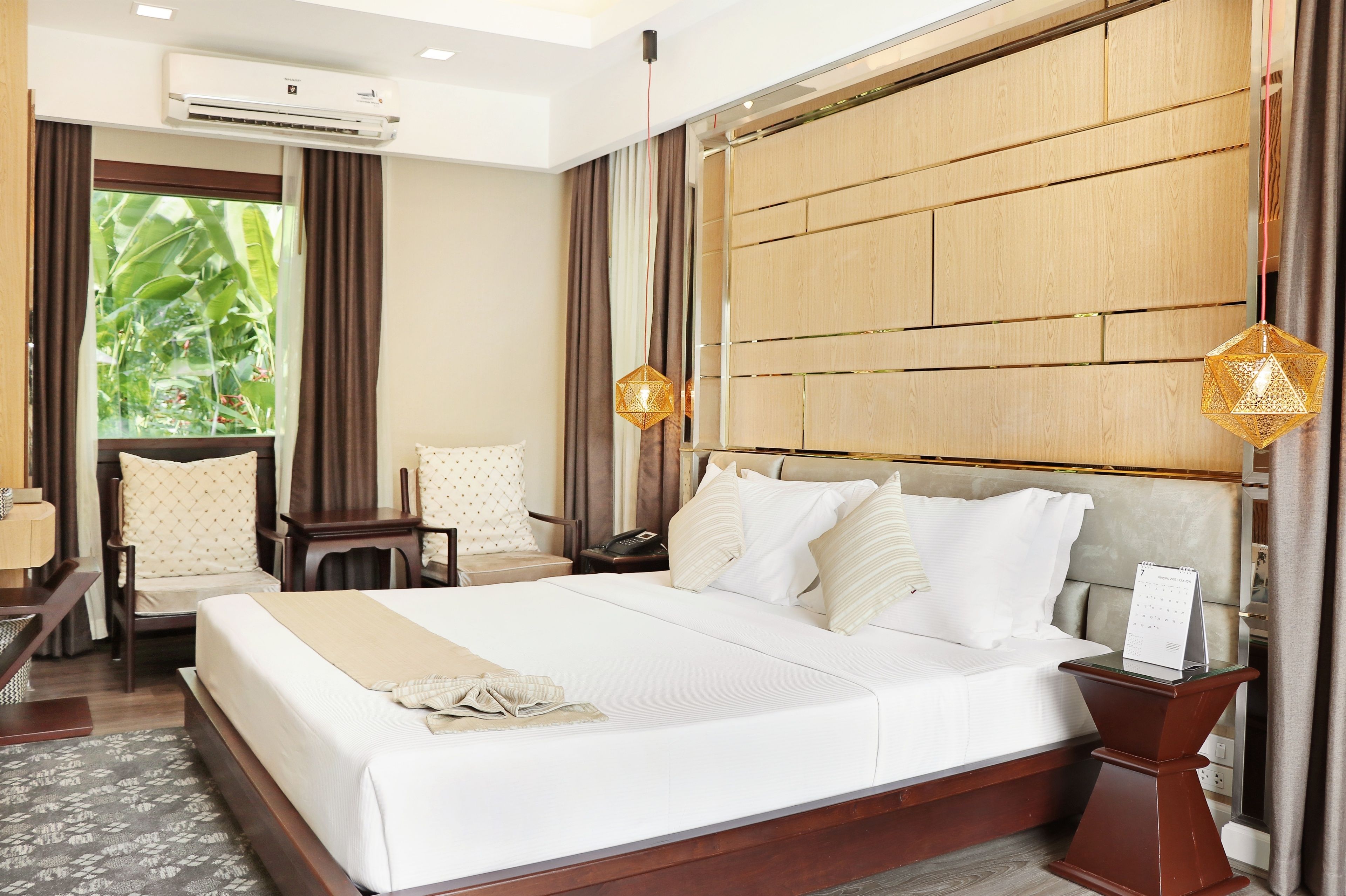 Een hotelkamer met een groot bed, een bureau, een stoel, een nachtkastje en een airconditioning.