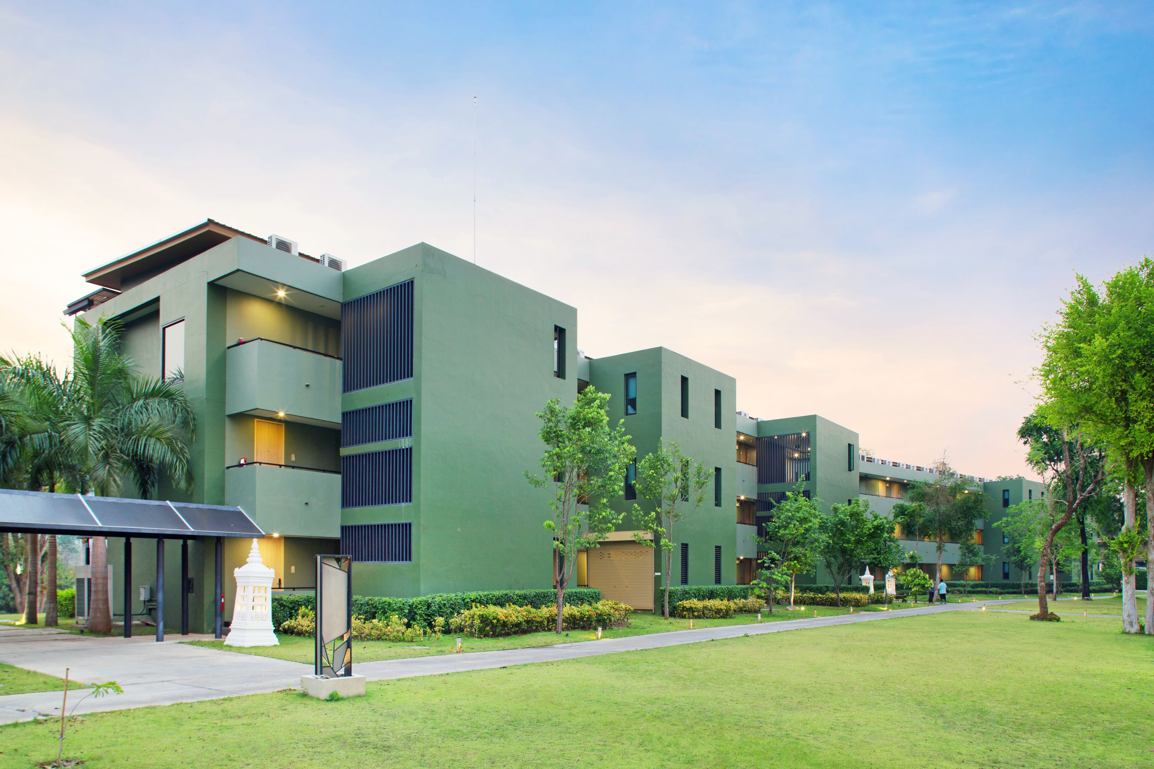A modern building with a flat roof, multiple balconies, and a well-maintained lawn with trees.