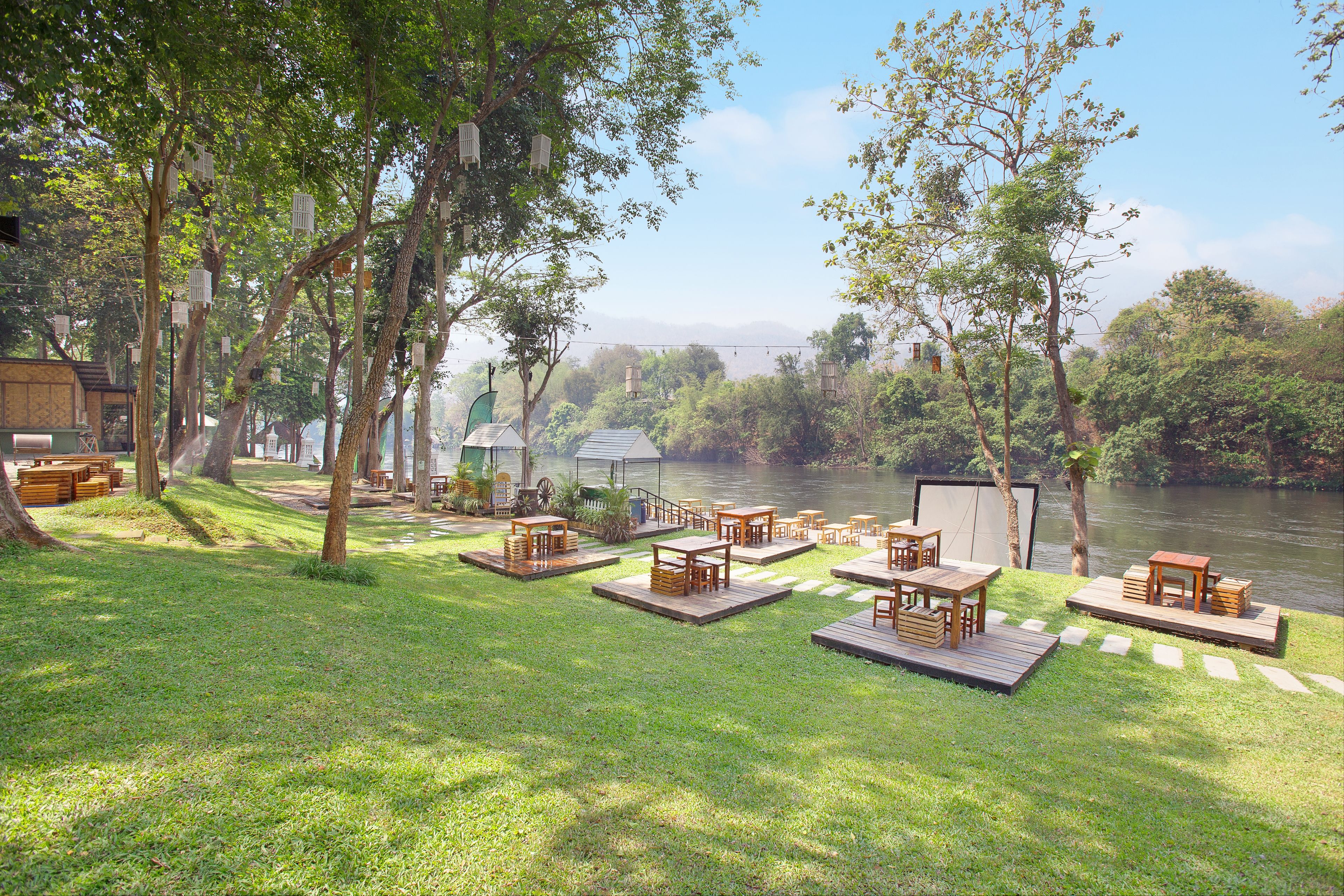 Un espace extérieur aménagé avec des tables et des chaises en bois, entouré d’arbres et offrant une vue sur une rivière.