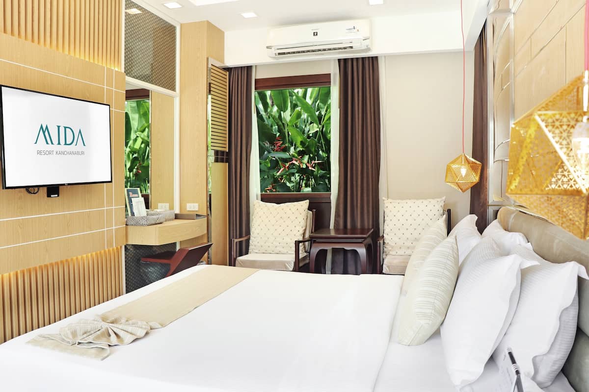 A hotel room with a large bed, a TV mounted on the wall, a window with curtains, and a small table with a chair.