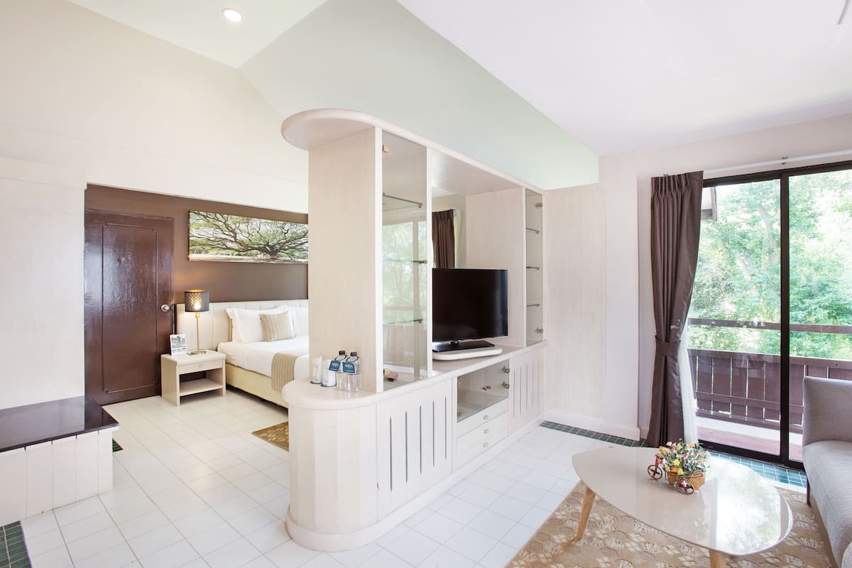 A modern hotel room with a bed, a TV, a sofa, a small table, and a balcony with a view.