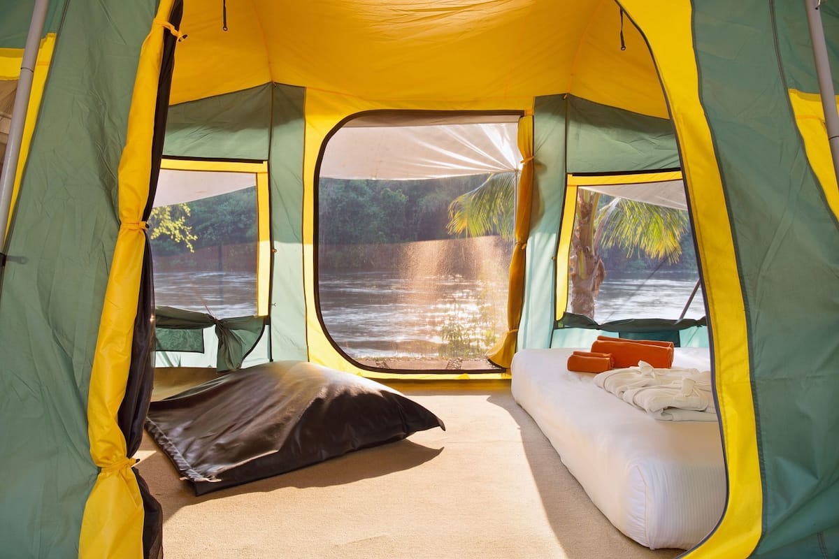 A tent with a bed, pillows, and a view of a river.