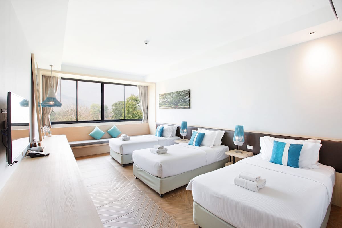 A hotel room with two beds, a large window, a TV, and a seating area with a view.