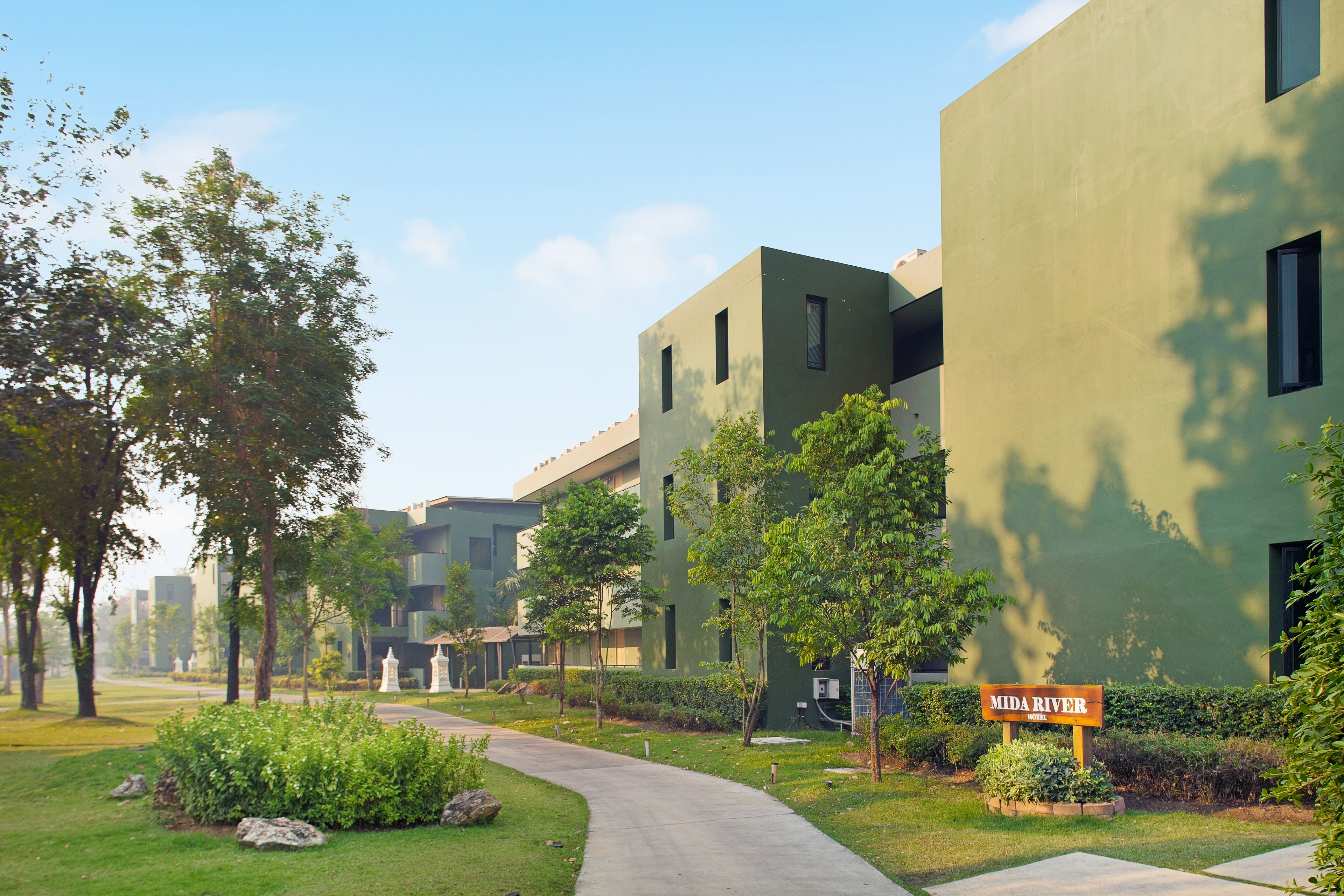 A modern hotel with a green facade, a paved walkway, and a sign reading "Mida River Hotel".