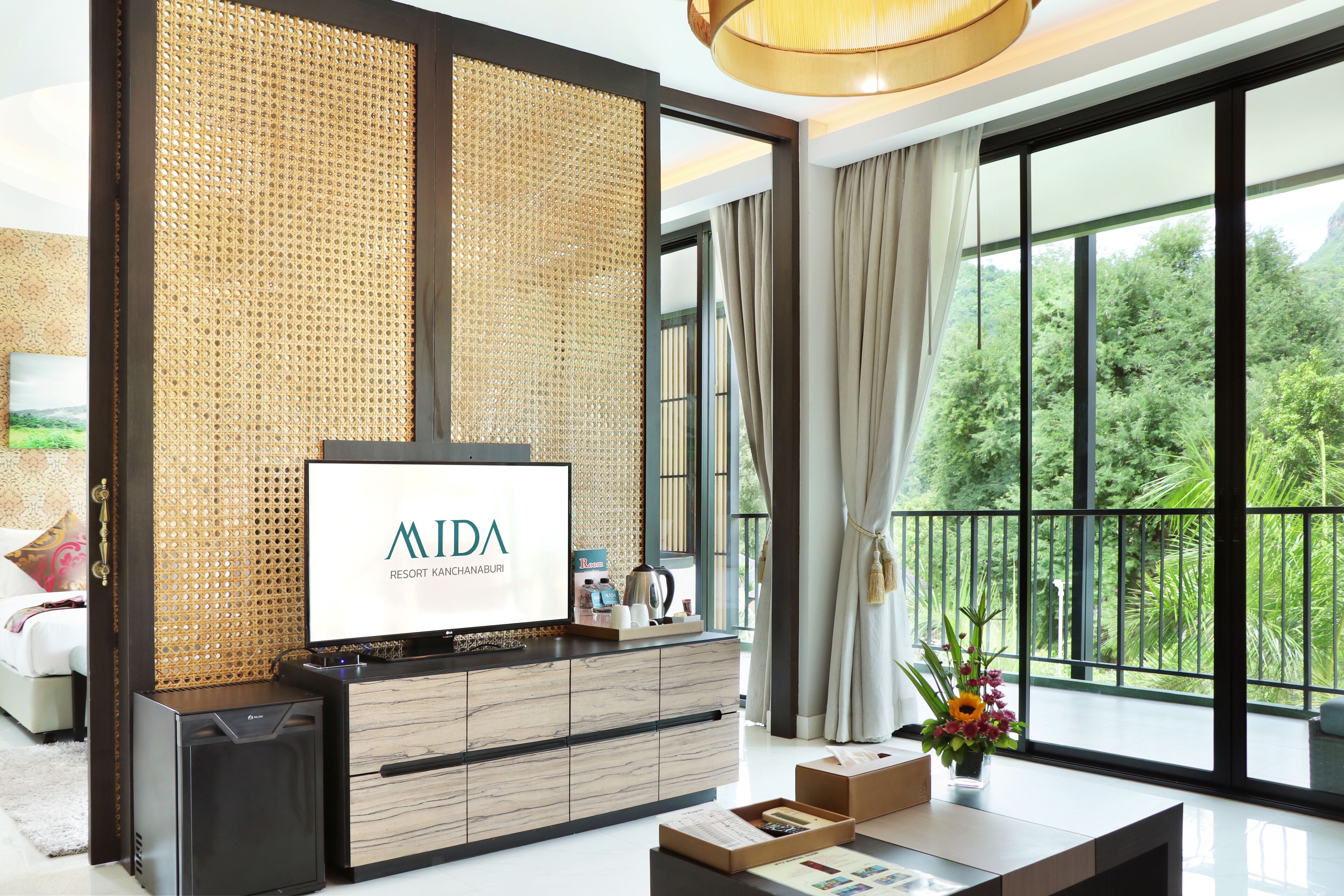 Una moderna camera d'albergo con una grande finestra, una TV a schermo piatto, un mobiletto in legno e un balcone affacciato sul verde.