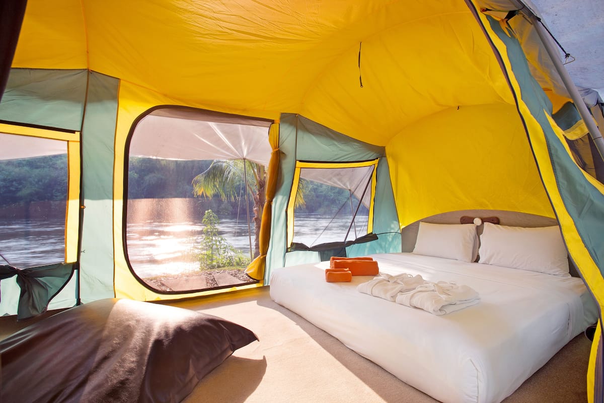 A tent with a bed, pillows, and a view of a body of water.
