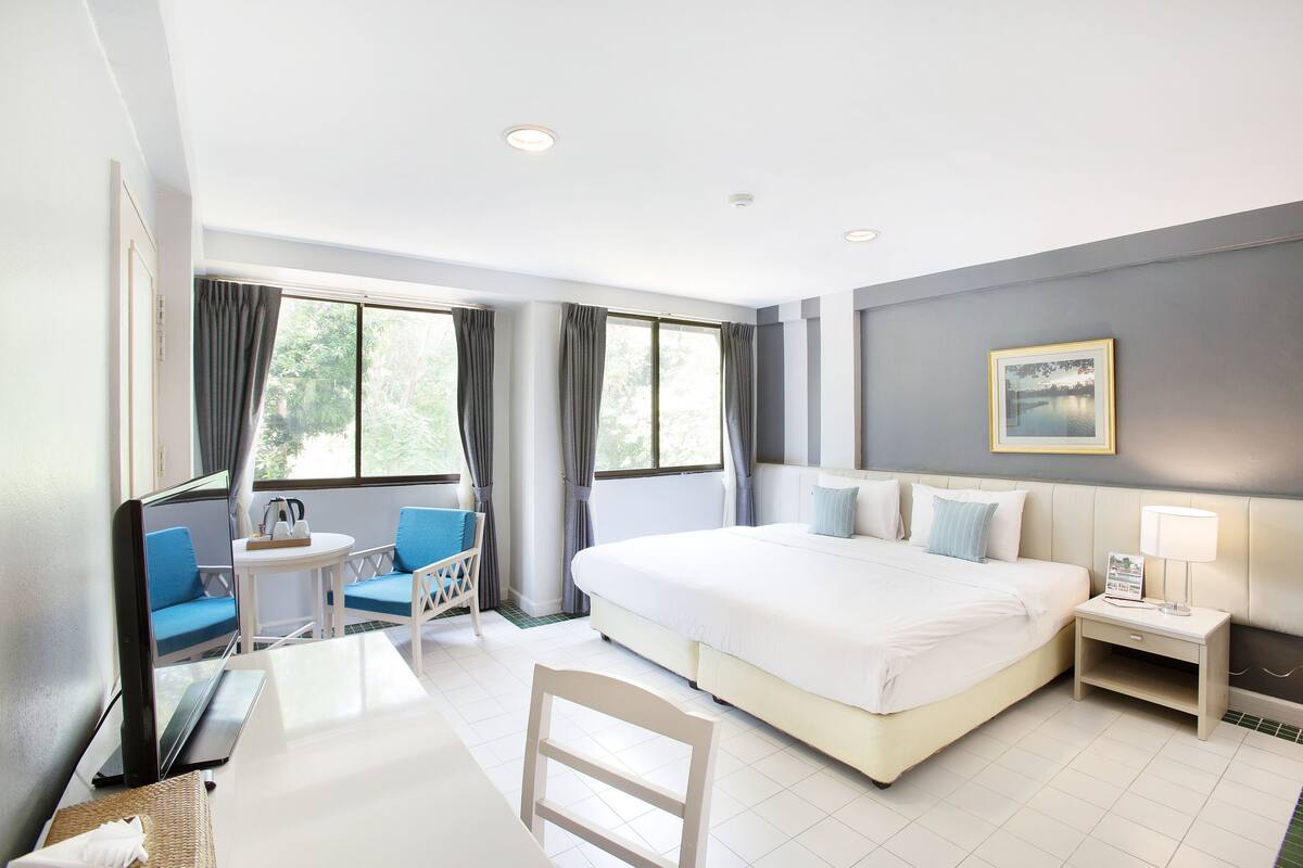 A hotel room with a large bed, a desk with a chair, a small table, and a window with curtains.