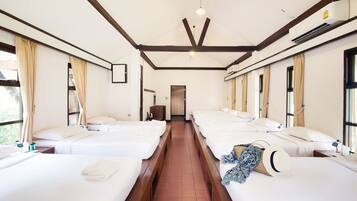 A hotel room with four single beds aligned in a row, a wooden ceiling, and large windows with curtains.