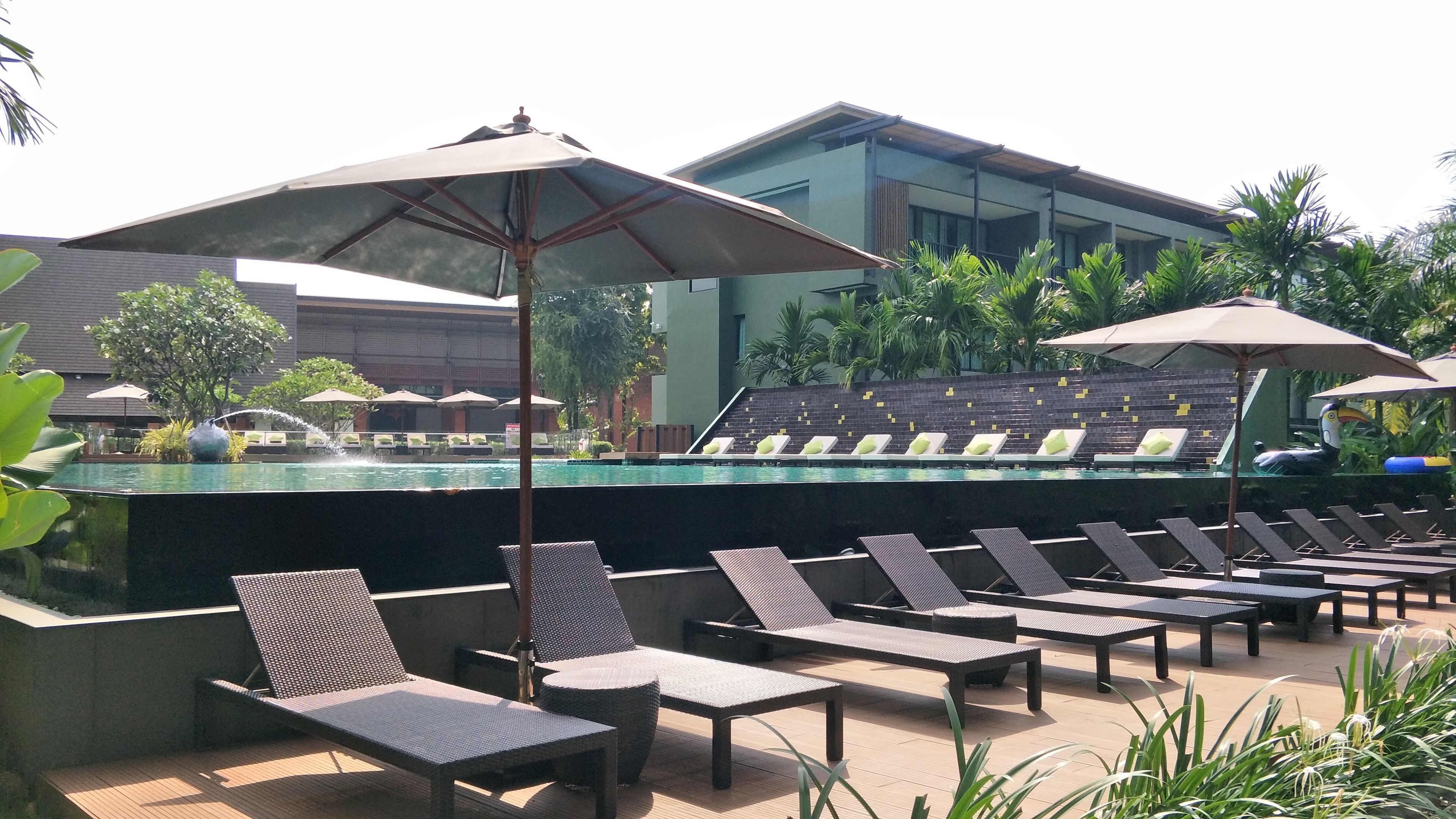 A poolside area with lounge chairs and umbrellas, a pool, and a modern building in the background.