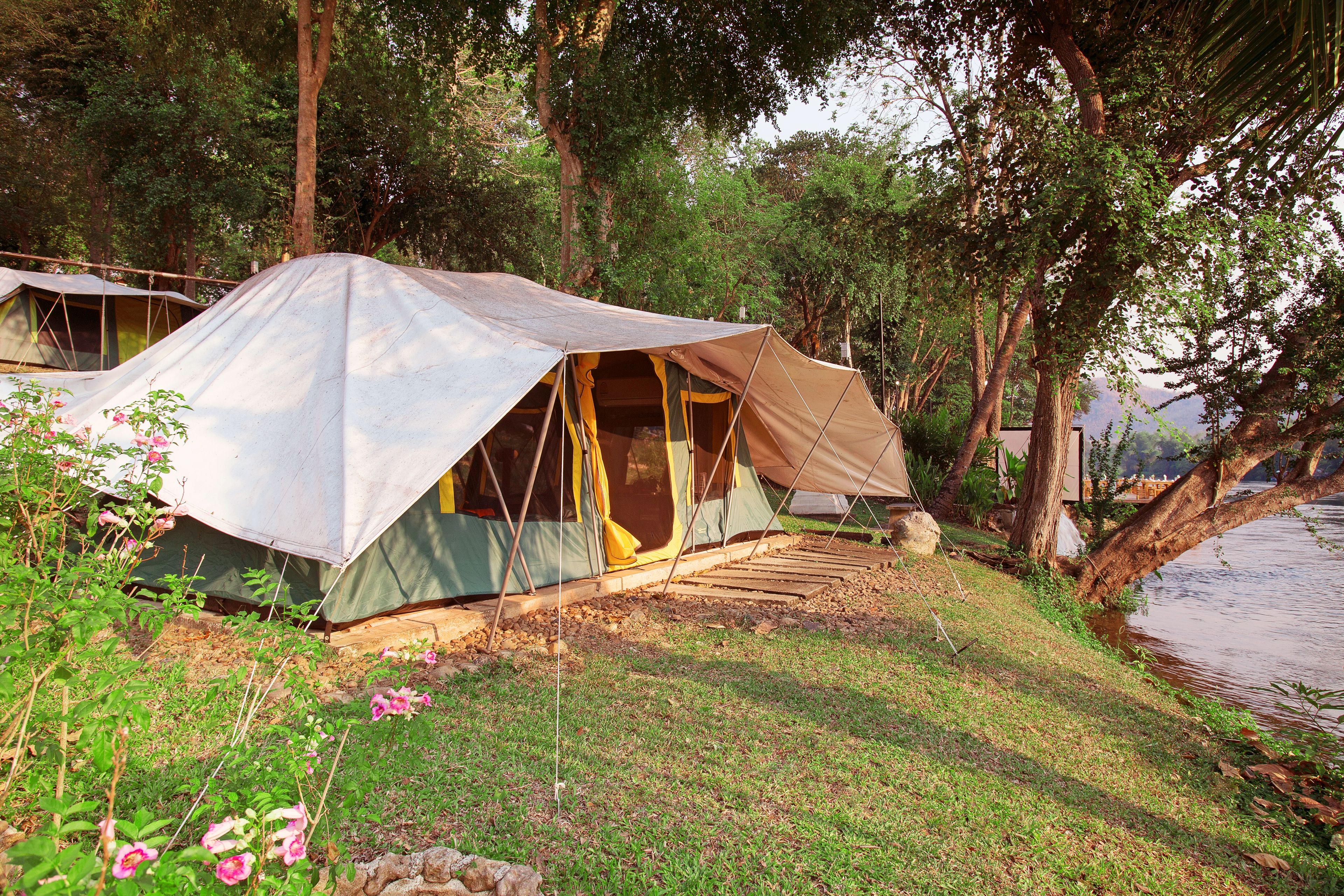 Un espace de camping aménagé avec des tentes, avec une rivière et des arbres en arrière-plan.