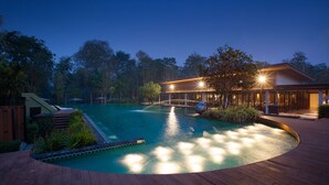 A swimming pool with a wooden deck, surrounded by trees and a building with outdoor seating. - Mida Resort Kanchanaburi (Kanchanaburi)
