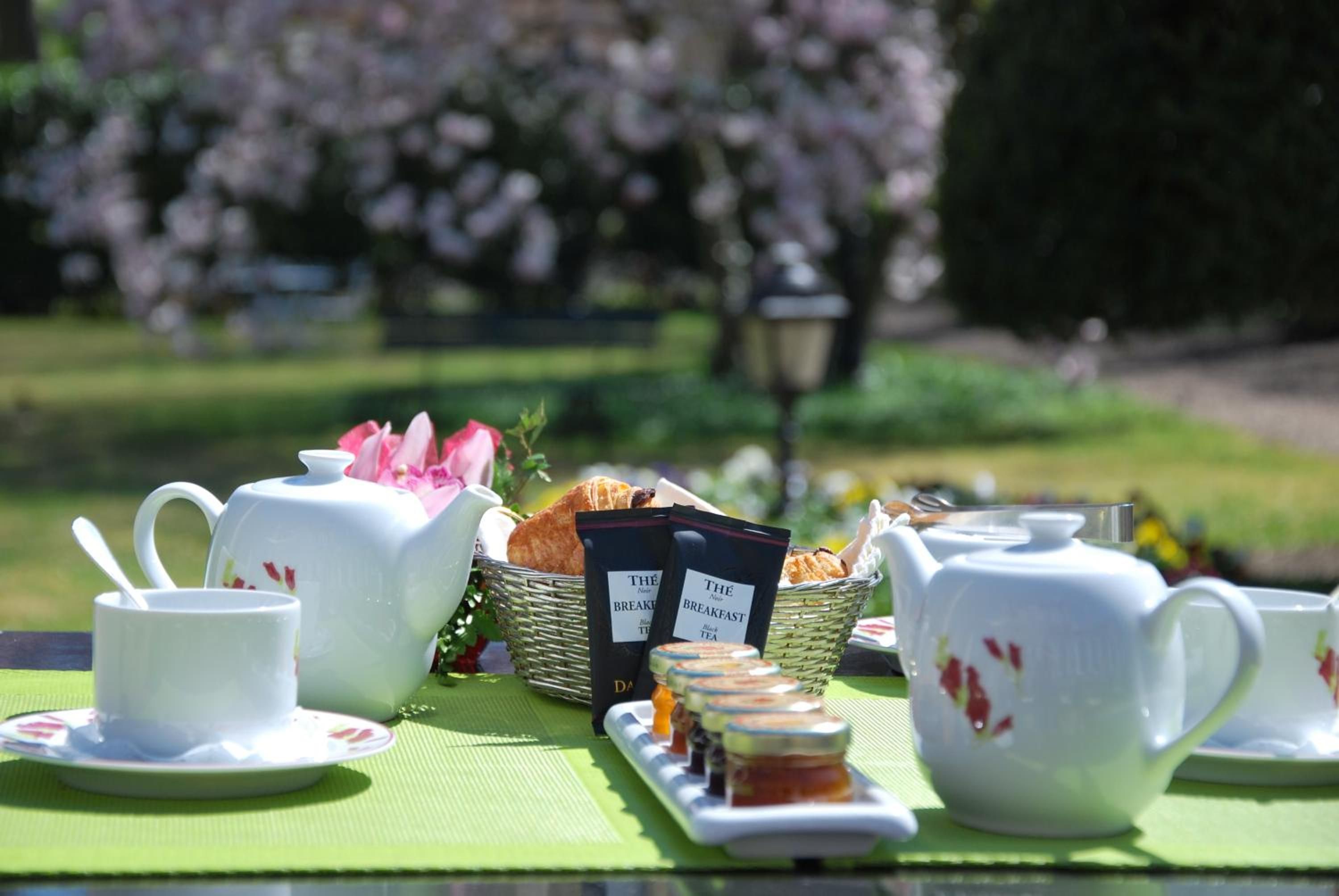 A picnic setup with a teapot, cups, a basket of bread, and tea packets on a table.