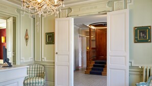 A room with a checkered armchair, a white door leading to a staircase, and a chandelier. - Le Clos De Bourgogne (Moulins)