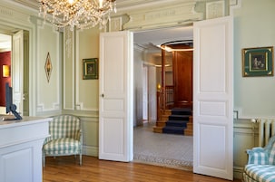 Una habitación con un sillón a cuadros, una puerta blanca que da a una escalera y un candelabro.