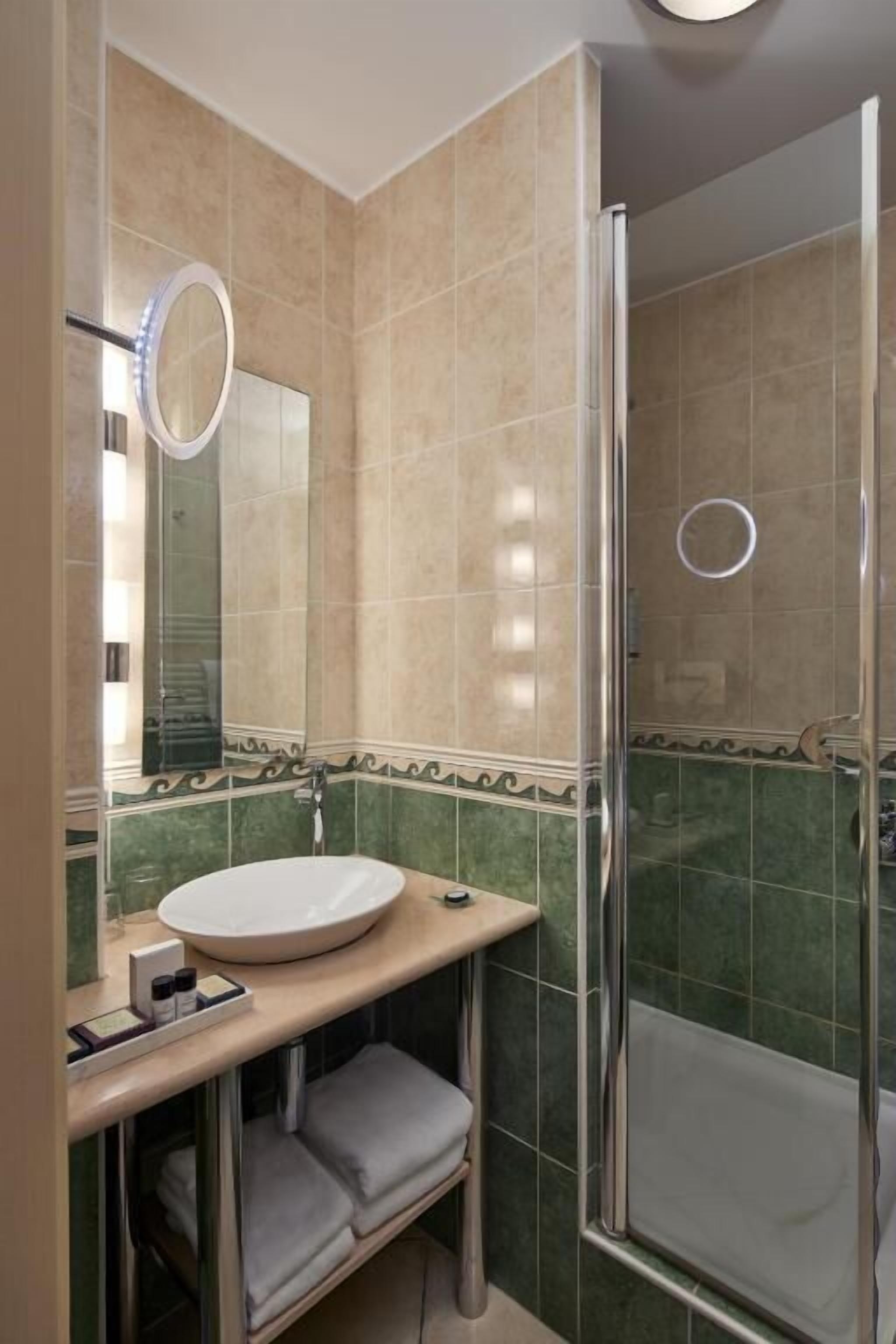 Een badkamer met een douche met glazen wand, een ronde spiegel en een wastafel met onderkast.