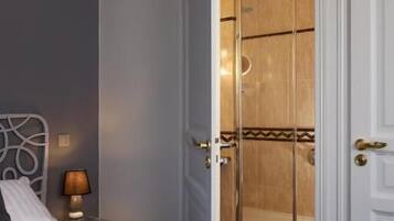 A hotel room with a bed, a bathroom with a shower, and a door with a golden handle.