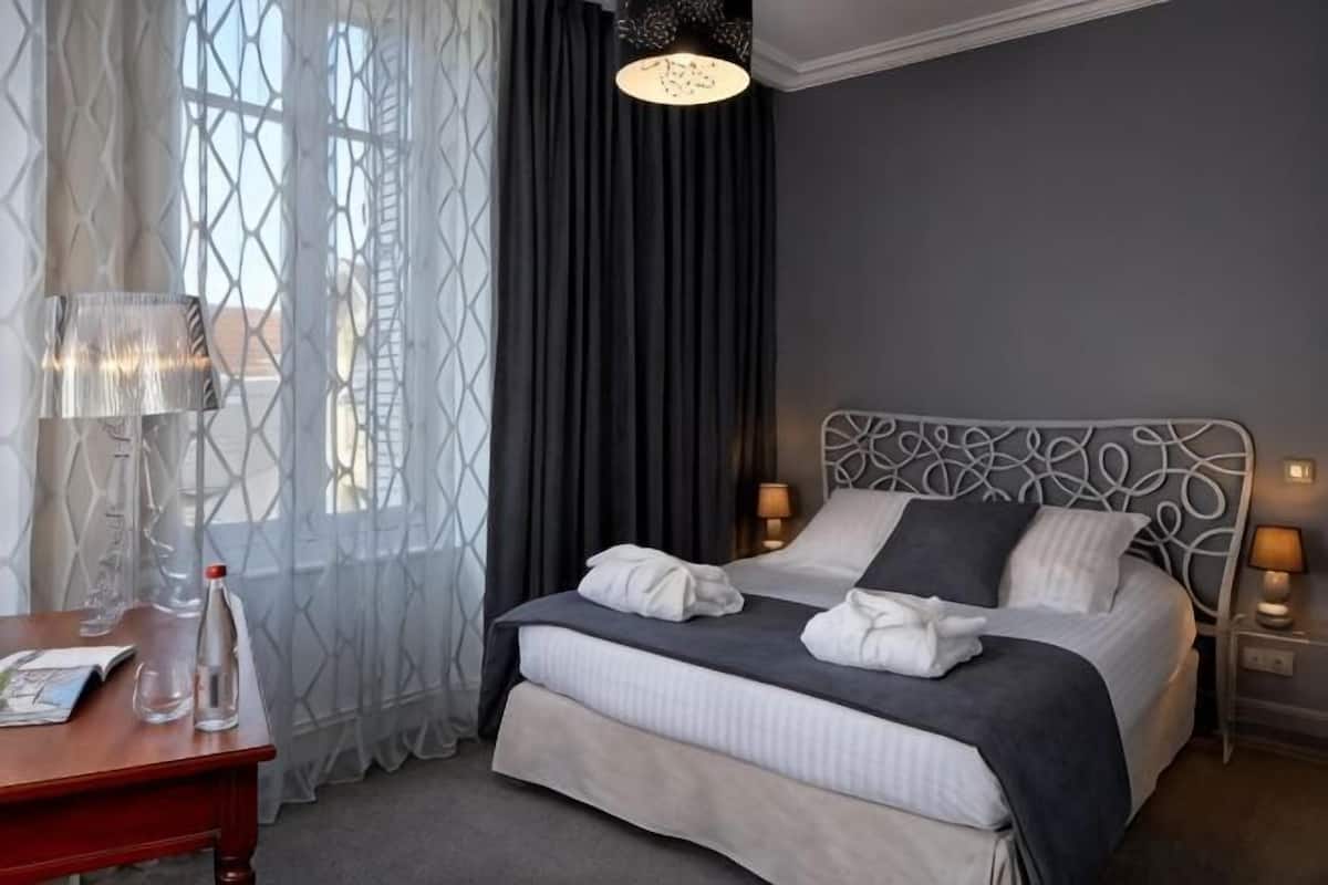 Una cama bien hecha con almohadas, una mesita de noche con lámpara y una ventana con cortinas.