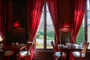 Un comedor con cortinas rojas, una mesa dispuesta con platos, tazas y una lámpara.