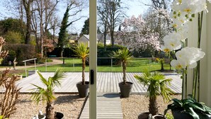 A wooden deck with potted plants, a view of a garden with trees and a lawn, and a white orchid in the foreground. - Le Clos De Bourgogne (Moulins)