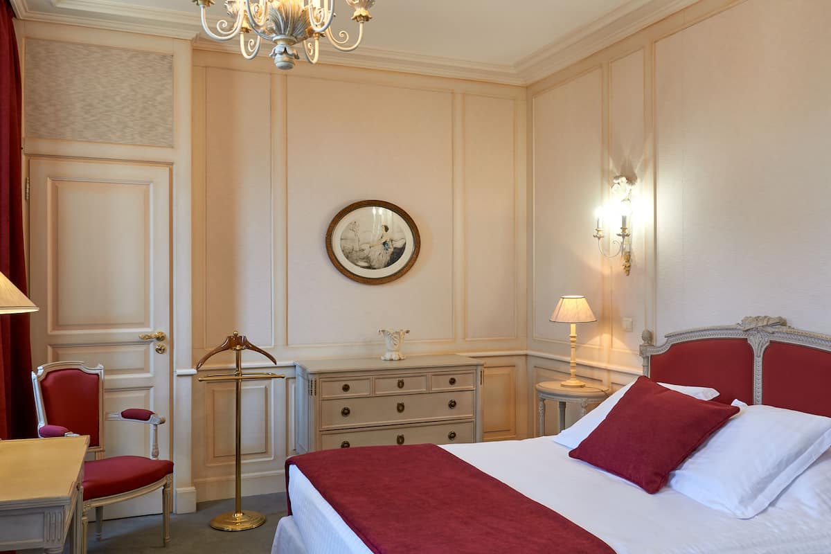 Habitación de hotel con una cama grande, un aparador, una silla, un escritorio y una araña.