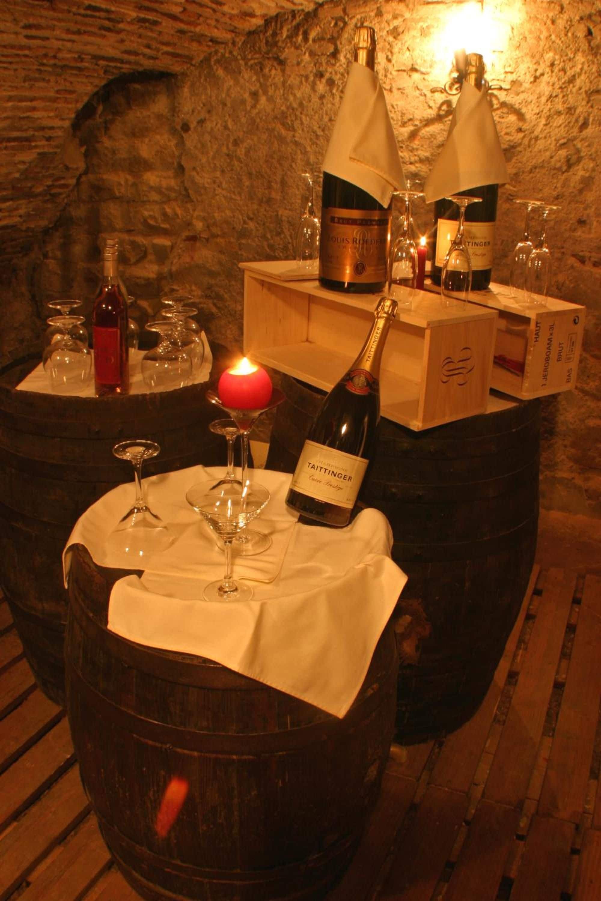 Una mesa de madera con un barril, una botella de vino Taittinger, una vela encendida y varias copas de vino.