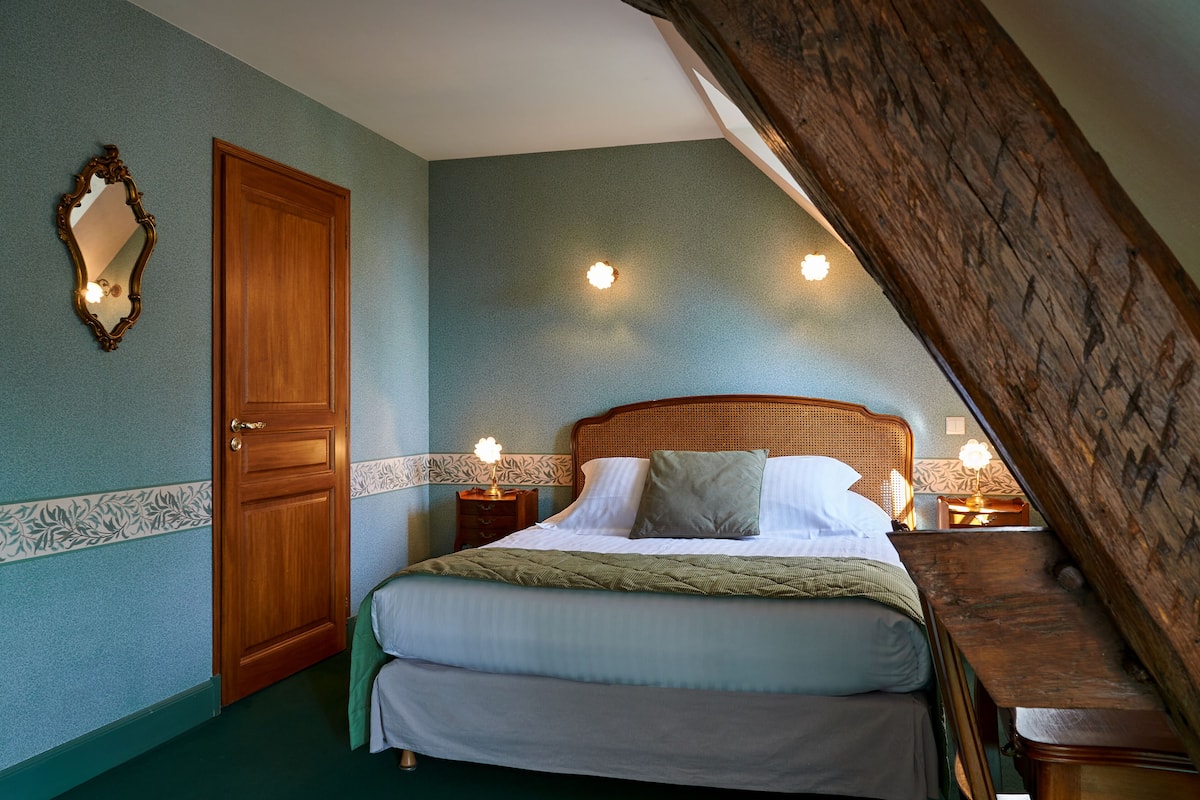 Un dormitorio con una cama de madera, dos mesitas de noche con lámparas, un espejo y una puerta.