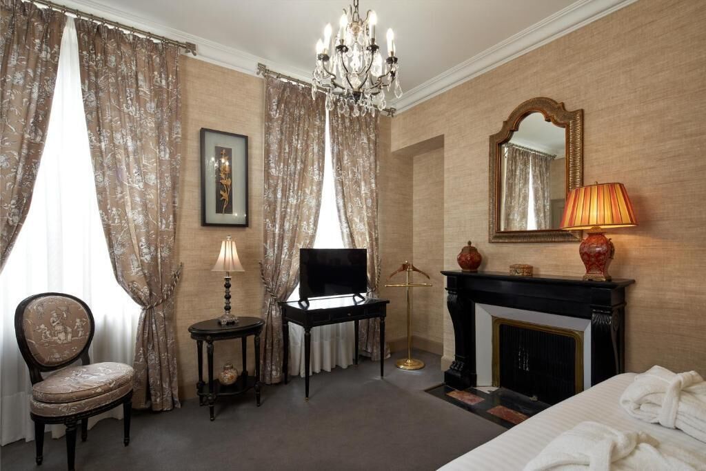 A hotel room with a bed, a television, a fireplace, a chair, and curtains.