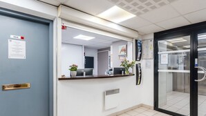 A reception area with a blue door, a reception desk with a computer, a plant, and a glass door leading to an elevator. - Sejours & Affaires Nantes La Beaujoire (Nantes)