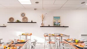 A modern dining area with multiple tables and chairs, featuring breakfast items and decorative wall art. - Sejours & Affaires Nantes La Beaujoire (Nantes)