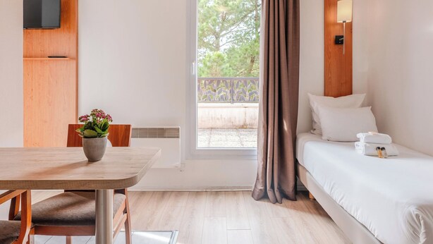 A hotel room with a bed, a bedside table with a lamp, a TV mounted on the wall, and a window with curtains. - Sejours & Affaires Nantes La Beaujoire (Nantes)