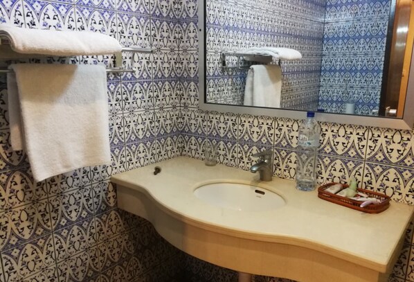 A bathroom with patterned tiles, a sink, a mirror, and a towel rack.