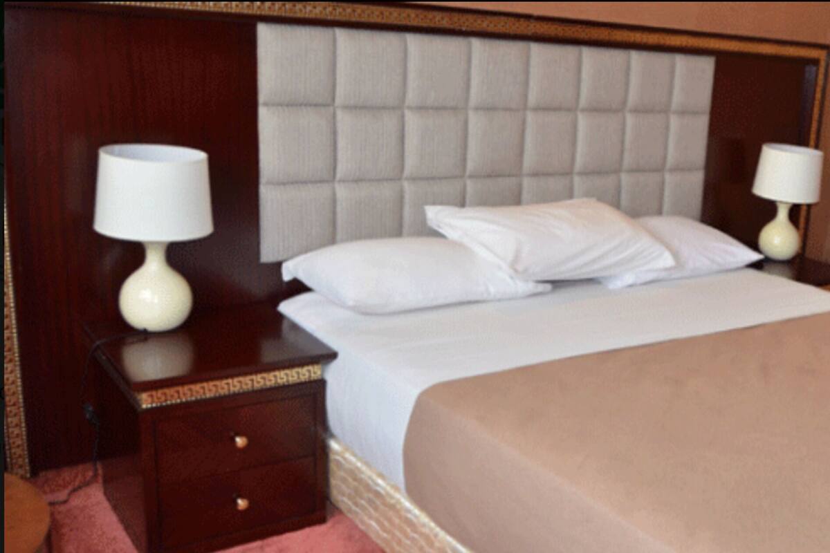 A neatly made bed with a headboard, two bedside tables with lamps, and a wooden nightstand.